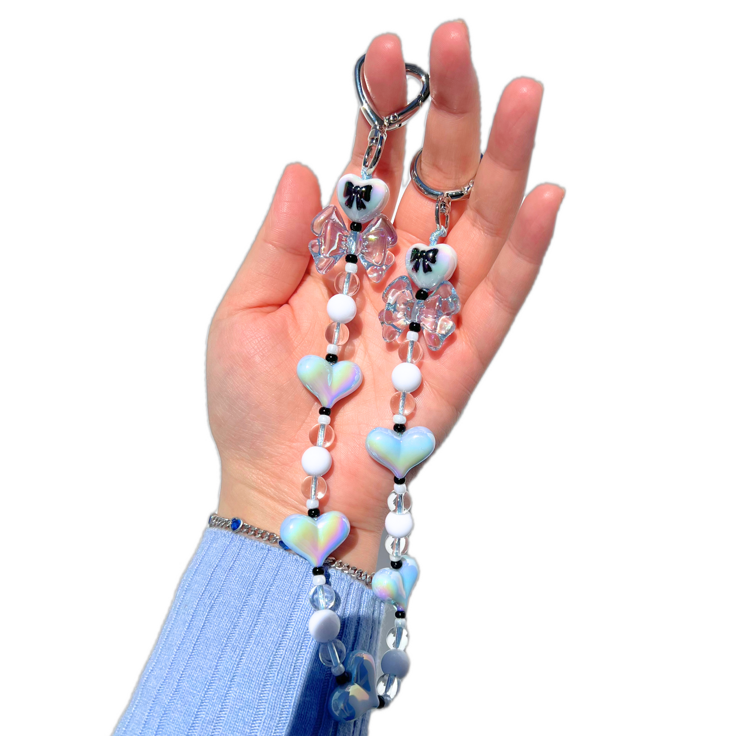 Handmade coquette kpop style baby blue heart and bow bag charm with iridescent beads and silver hardware held in hand.