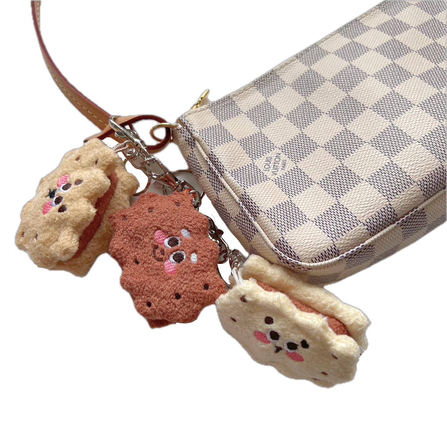 Sandwich cookie plush keychains clipped to a designer checkered purse, showing textured cookie shapes and playful embroidered faces.