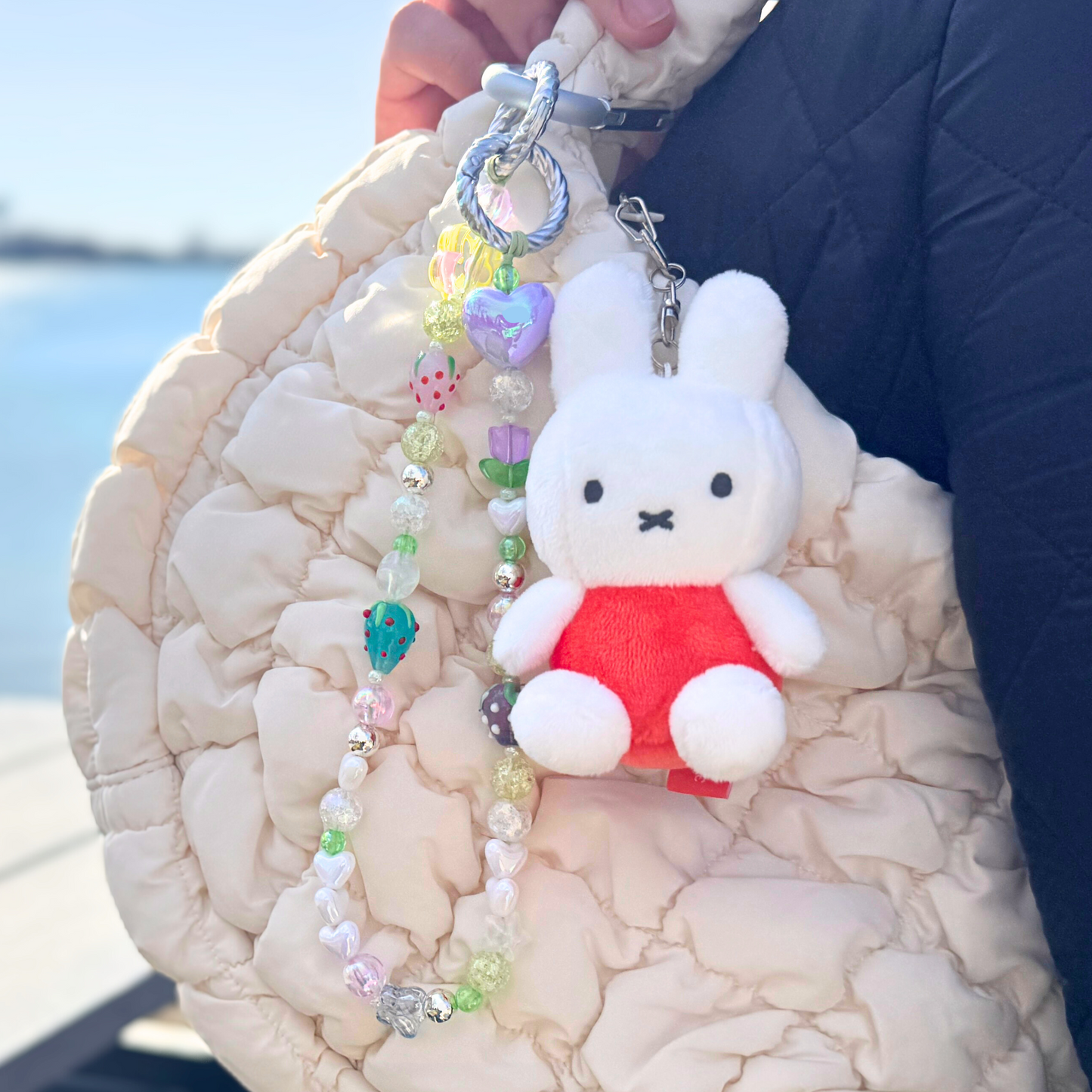 Handmade bag charm clipped onto a quilted cream handbag next to a plush Miffy keychain. The beaded charm features soft pastel colors and fruit-inspired beads for a playful, aesthetic look.