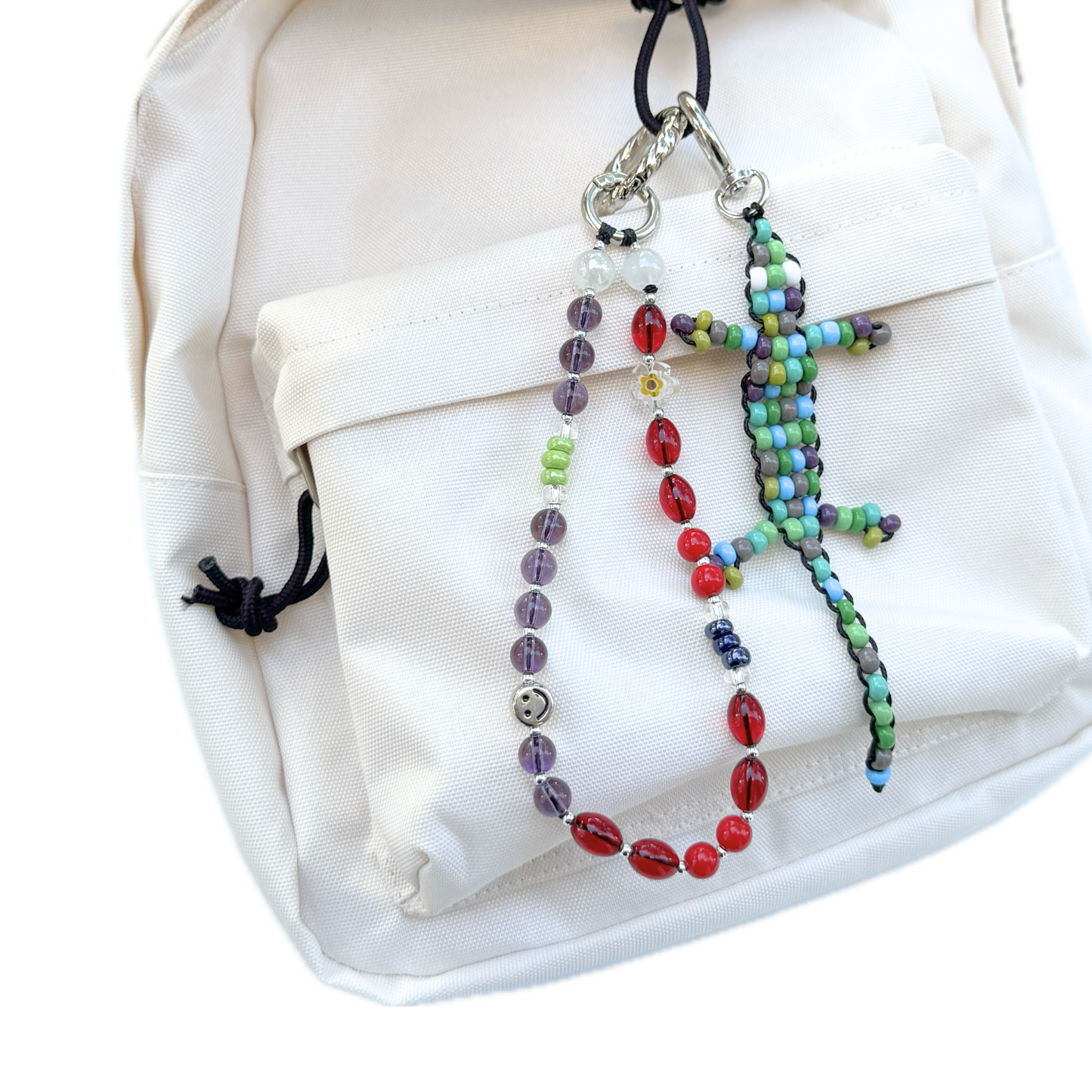Beaded Green Gecko Bag Charm attached to a white backpack alongside other beaded charms, showing its colorful handmade lizard design in use.