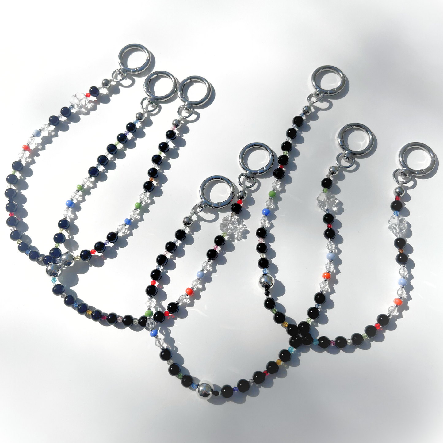 Multiple Black Orbit Beaded Bag Charms arranged on a white background, showcasing their glossy black beads, clear crystal accents, and colorful details under bright light.