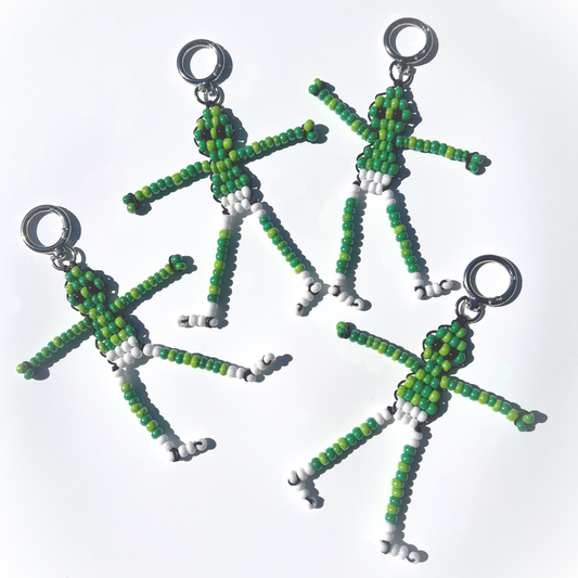 A flat lay of multiple Beaded Green Martian Bag Charms made with green, white, and black beads, each featuring silver-tone hardware and playful poses.