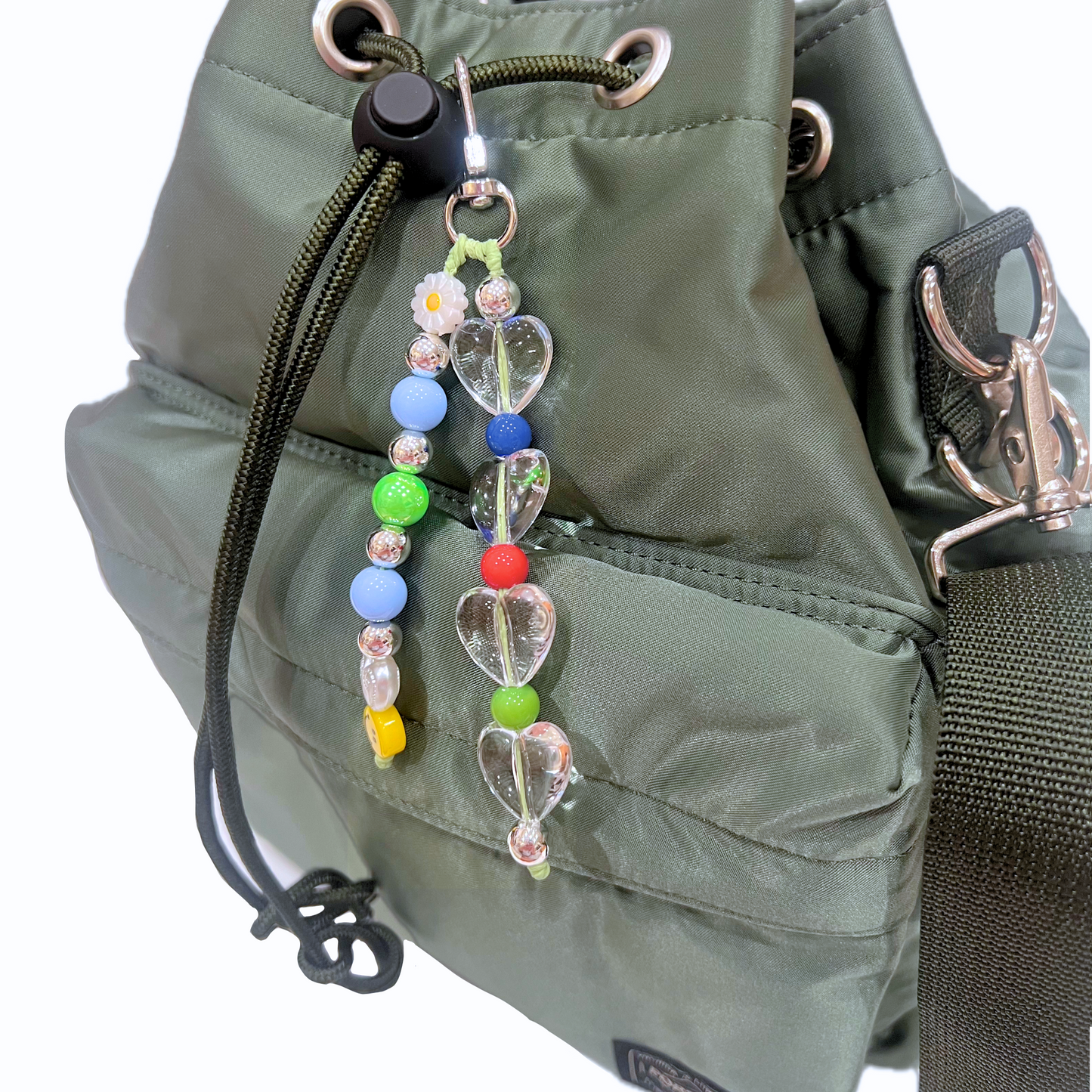 A cute happiness beaded keyring on a green nylon bucket bag, showing clear heart beads and colorful accents.