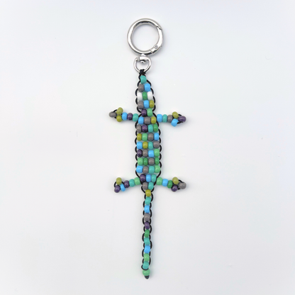 Single green, blue, and grey beaded gecko bag charm photographed front-facing on a white background with metal keyring.