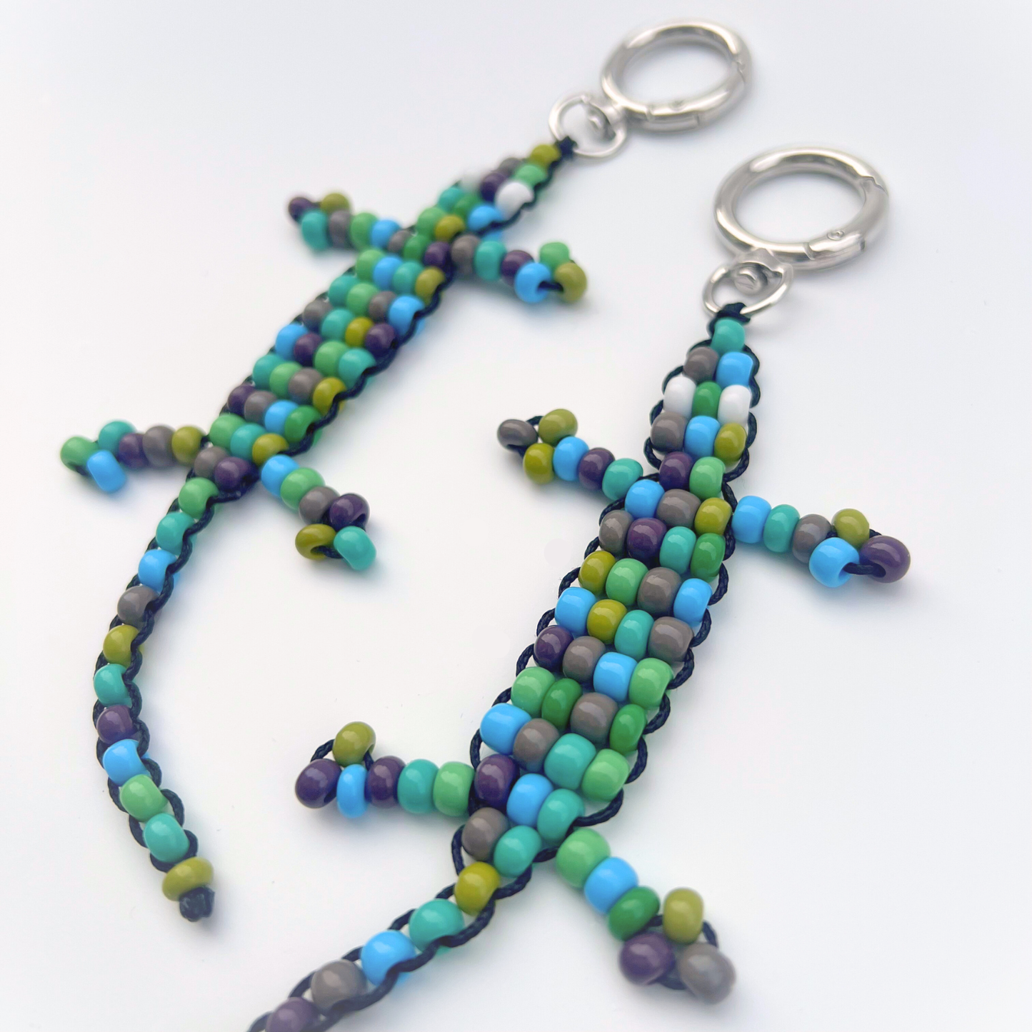 Close-up of green, blue, and purple beaded gecko bag charms showing detailed beadwork on a white background.