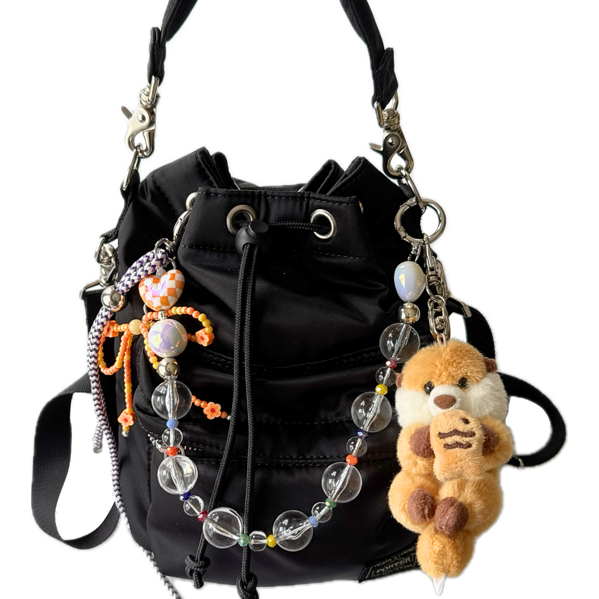 Black bag with decorative bag charms and keychain and plush otter. Kawaii bag decoration on display