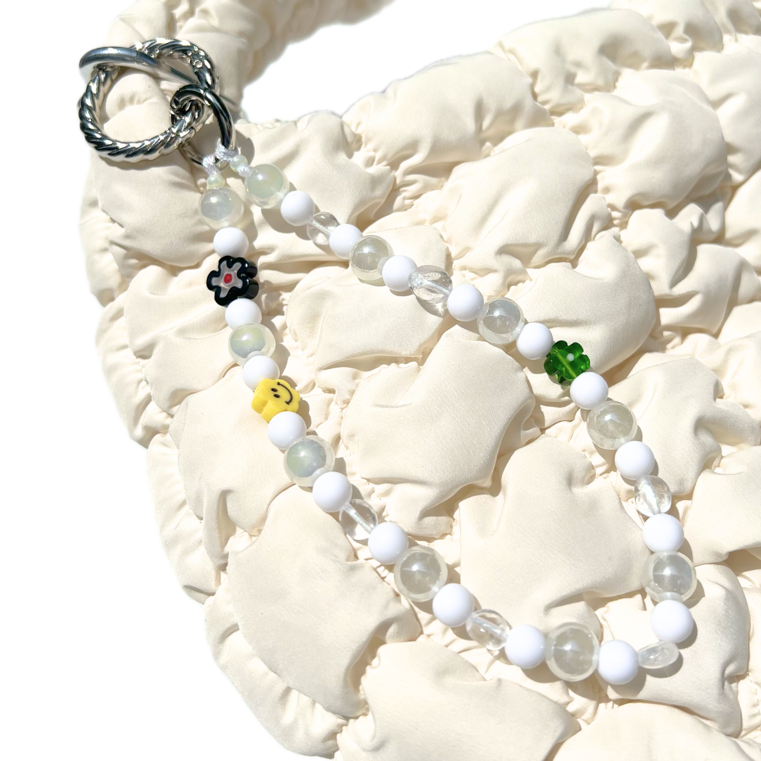 Luminous white eclectic beaded charm clipped to a cream quilted bag, featuring milky glass and clear beads with playful accents including a yellow smiley, green and black flowers. Handmade with glass, Czech, millefiori, and acrylic beads.