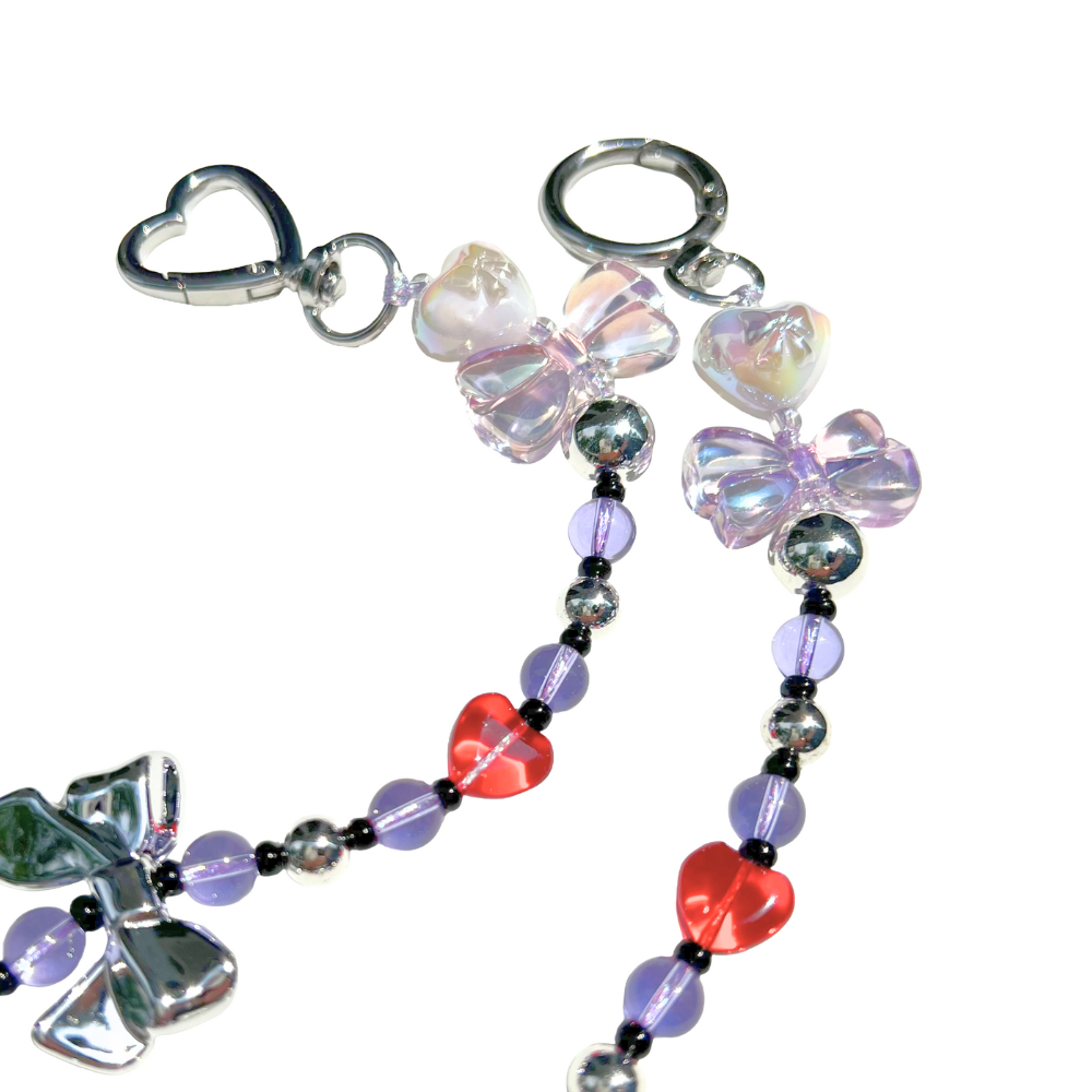Close-up of lilac magical girl beaded charm featuring iridescent bow beads, red heart accents, and chrome heart clasp hardware.