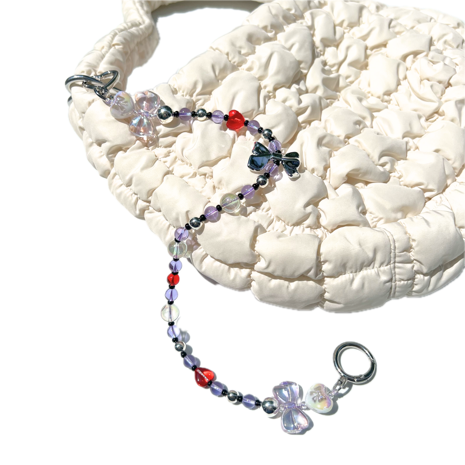 Lilac magical girl beaded charm with iridescent bows and red heart beads styled on a cream quilted handbag.