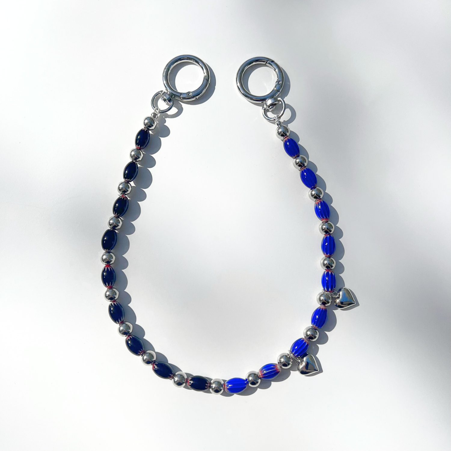Single Modern Romantic Beaded Bag Charm displayed on a white surface, showing alternating black and blue chevron glass beads with silver heart details and chrome clasp.
