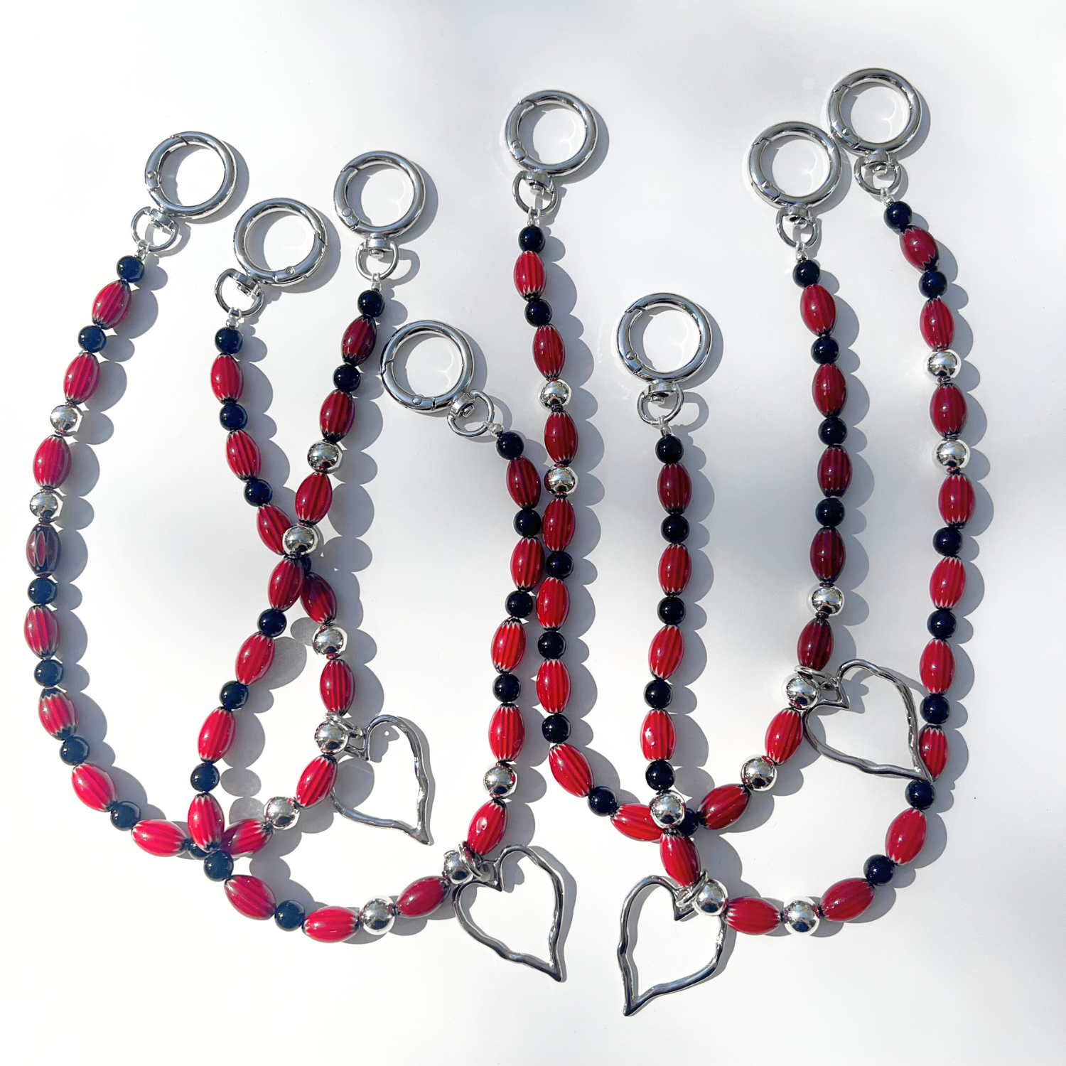 Set of Modern Romantic Beaded Bag Charms in black and crimson arranged together to show their silver heart pendants, red glass beads, and reflective chrome finish.