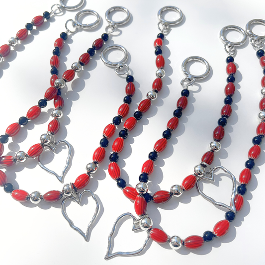 Close-up of multiple Modern Romantic Beaded Bag Charms featuring red chevron glass beads, glossy black beads, and silver heart pendants with chrome hardware on a white background.