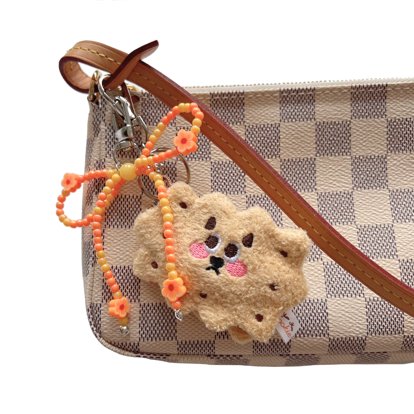 Honey sandwich cookie plush keychain clipped to a checkered designer purse, paired with an orange beaded bow charm featuring flower accents.