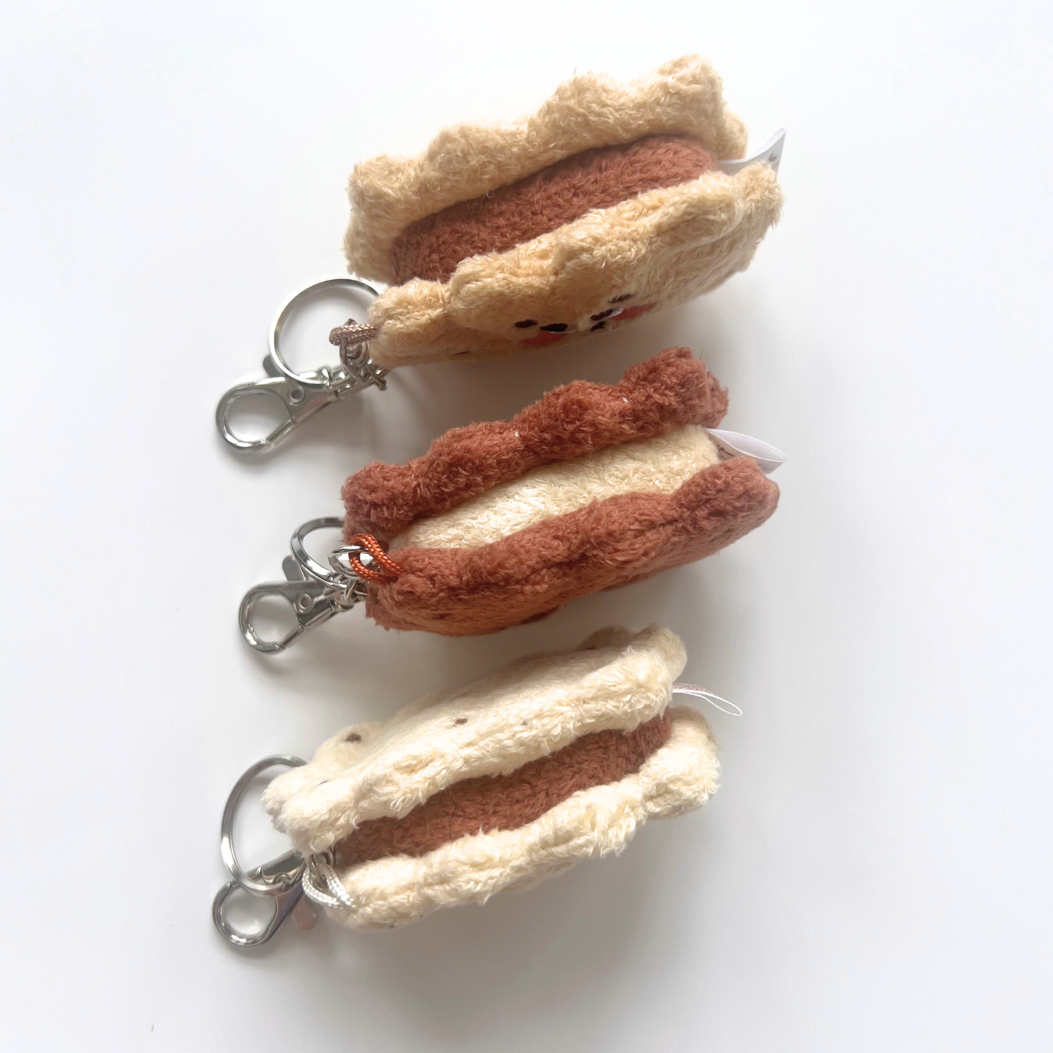 Side view of three sandwich cookie plush keychains, highlighting the layered biscuit and filling design with attached silver keychain hardware.