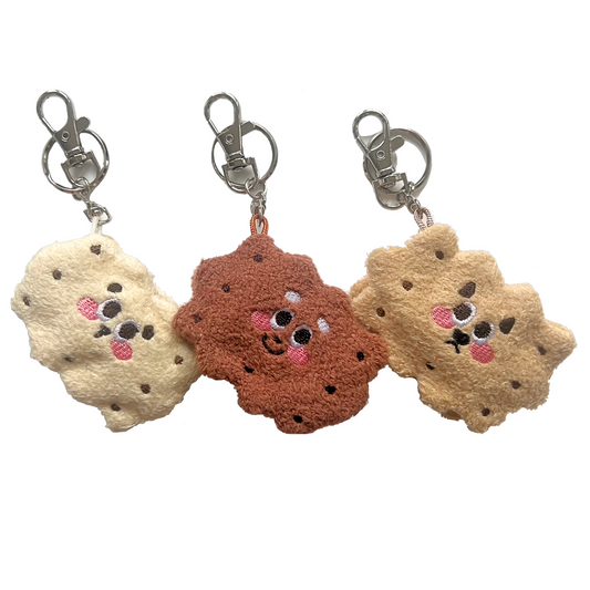 Front view of three sandwich cookie plush keychains in vanilla, chocolate, and honey styles, each with cute embroidered faces and silver lobster clasps.