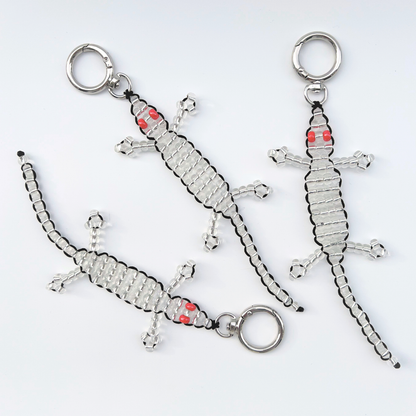 Three handmade silver beaded gecko bag charms with red eyes, shown laid flat on a white background with push clasp keyrings.