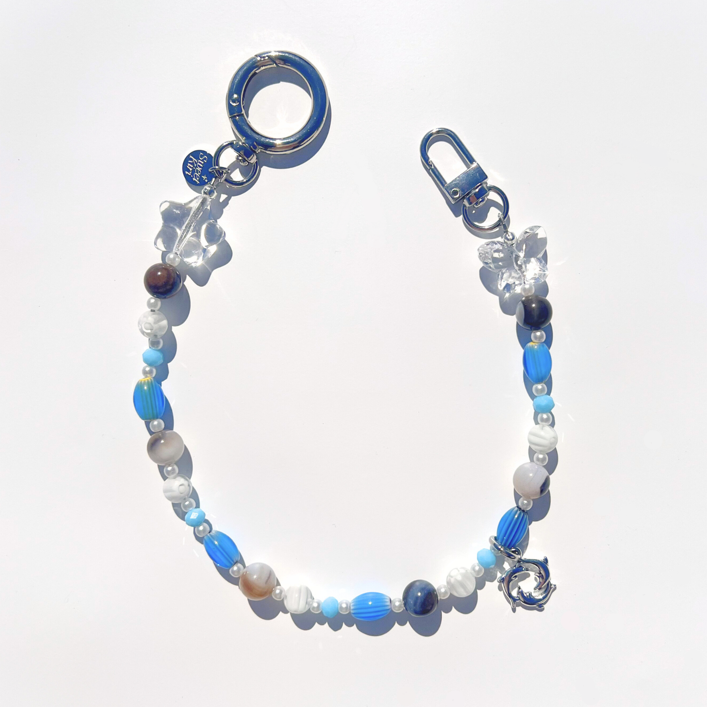 Coastal Muse Marina Blue bag charm with blue glass beads, agate stones, clear star and butterfly beads, and a triple dolphin ring pendant