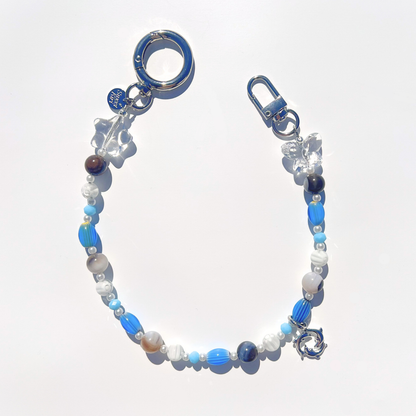 Coastal Muse Marina Blue bag charm with blue glass beads, agate stones, clear star and butterfly beads, and a triple dolphin ring pendant