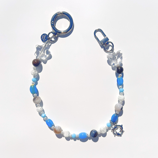 Coastal Muse Marina Blue bag charm with blue glass beads, agate stones, clear star and butterfly beads, and a triple dolphin ring pendant