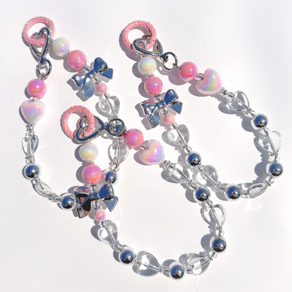 A close-up view of several Kawaii Pink Beaded Bag Charms, highlighting the reflective silver beads, iridescent hearts, and pastel pink accents glowing under sunlight.