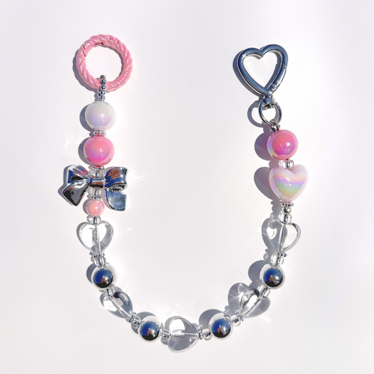 A single Kawaii Pink Beaded Bag Charm featuring pastel pink, iridescent white, and silver beads with heart and bow details, displayed on a white background under bright sunlight.