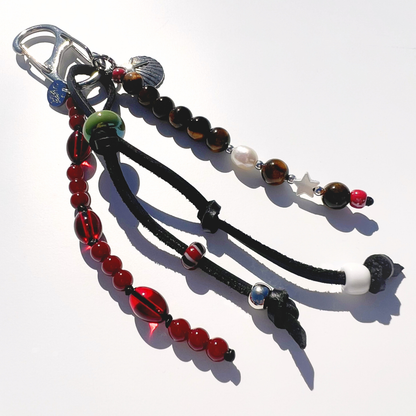 Close up of Mariner Relic Tiger Eye & Crimson bag charm showing tiger eye stones, red glass beads, leather cord knots, and starfish shell pendent 