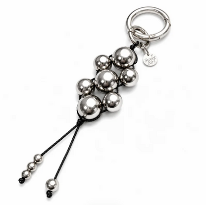 Close-up of the Modern Talisman Chrome Beaded Bag Charm with reflective chrome beads, handwoven black cord, and Sweet Kiri branded keyring.