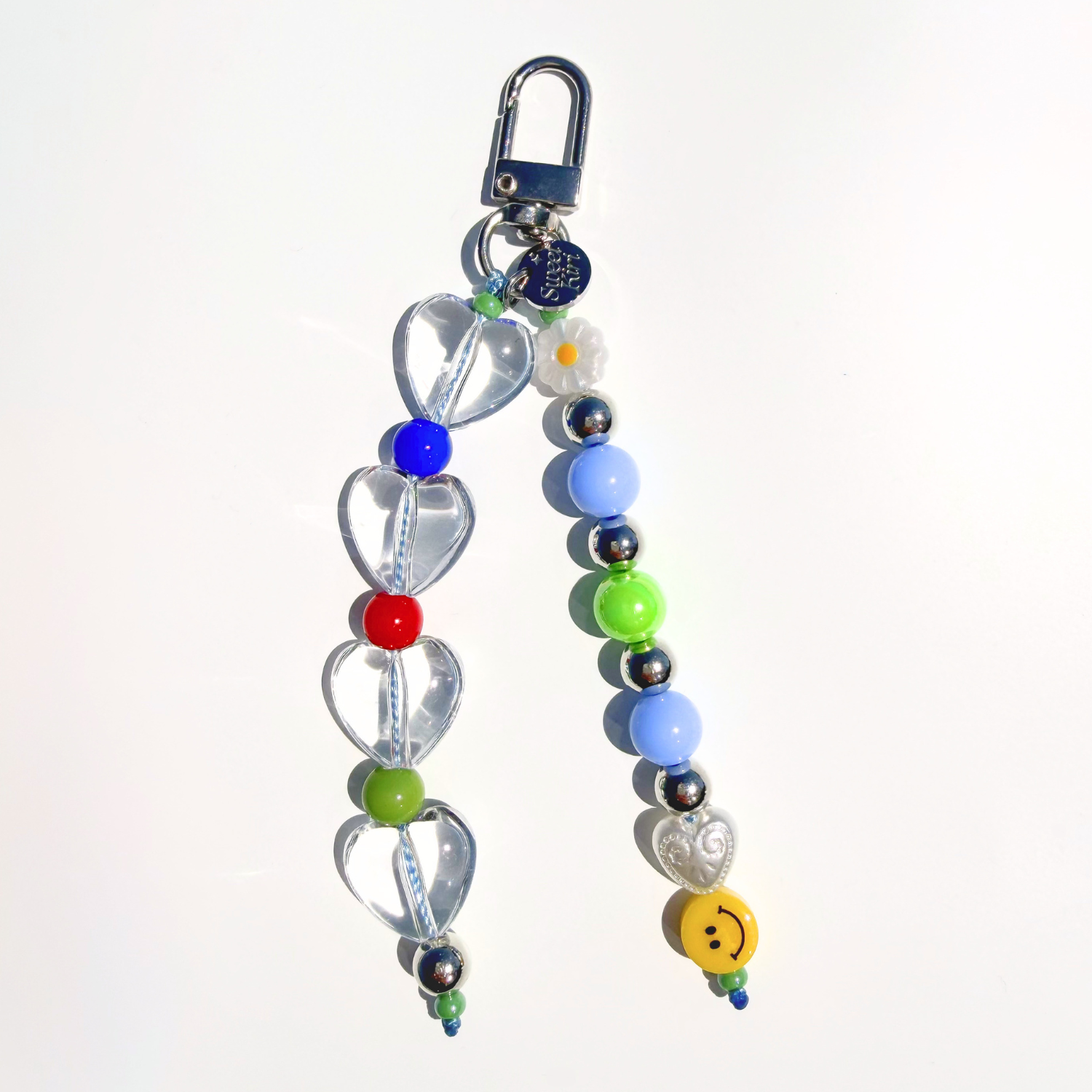Clear heart beaded bag charm with smiley face bead, daisy accent, and pastel beads on white background