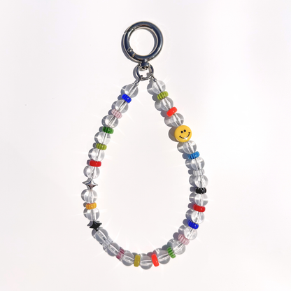 A single Solar Joy Beaded Bag Charm with clear beads, colorful rings, silver stars, and a yellow smiley bead, displayed on a white background under natural light.