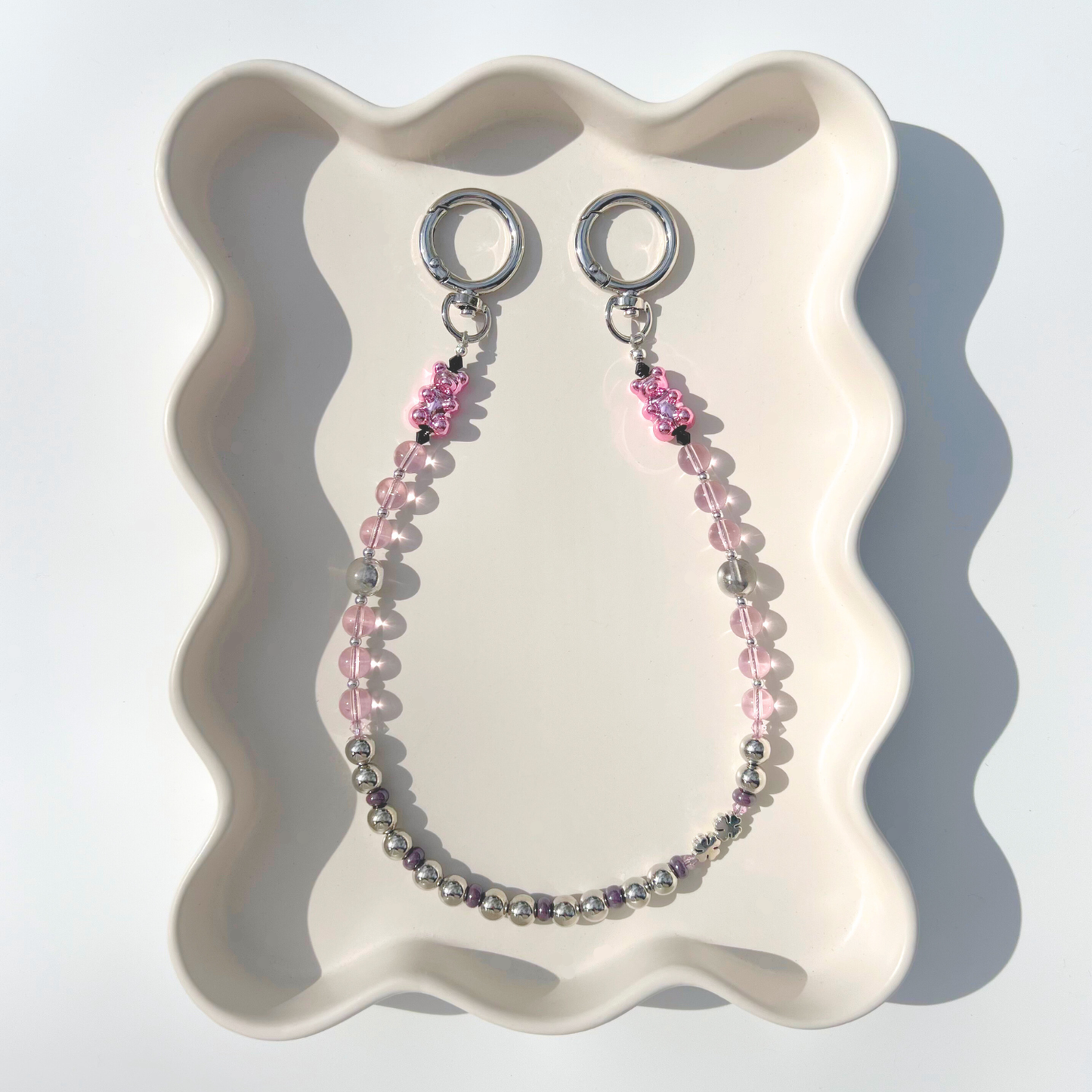 A pink glass bead and chrome bead bag charm with a gummy bear detail styled on a wavy ceramic tray.