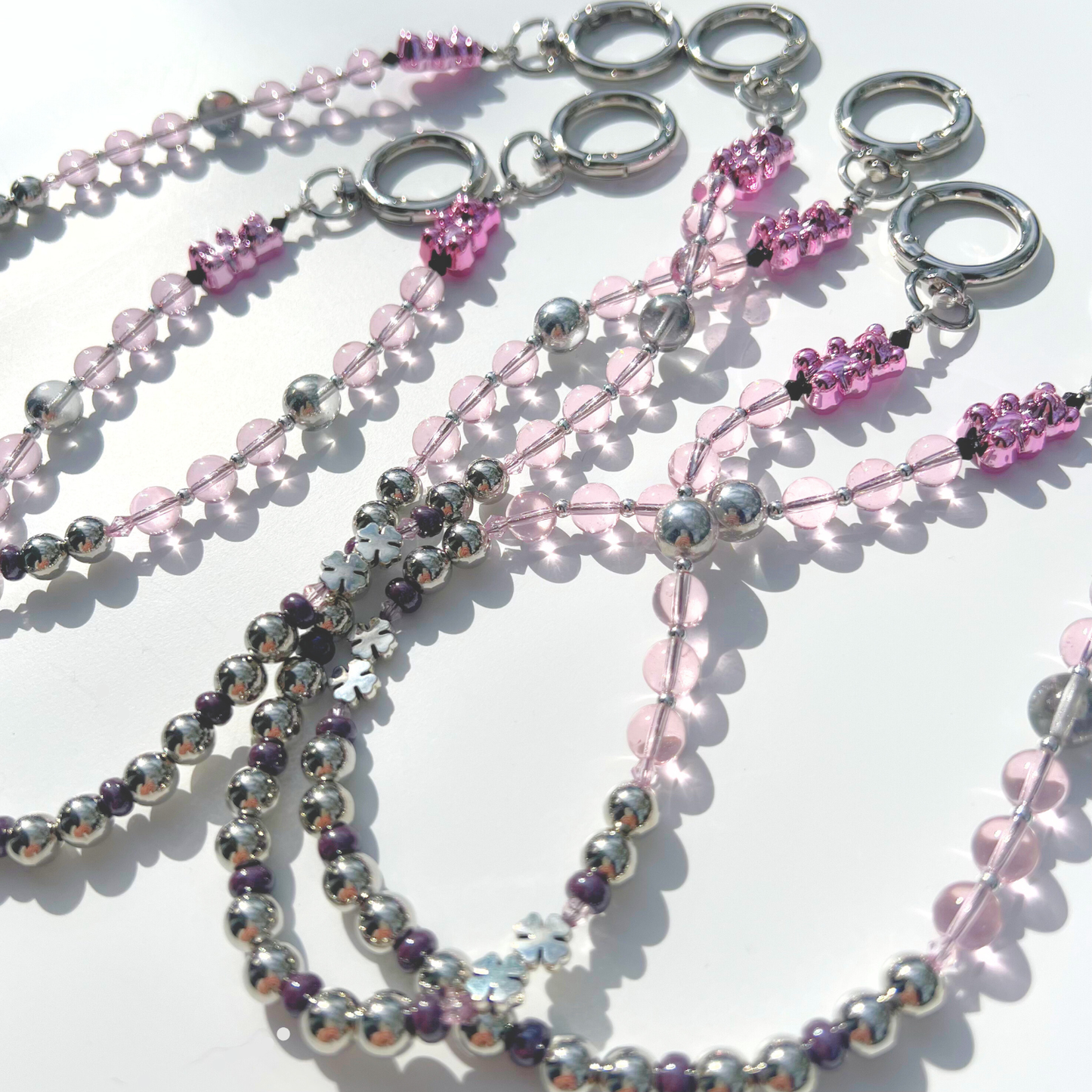 Multiple pink beaded bag charms arranged together, featuring pink glass beads, chrome beads, and pink gummy bear accents.
