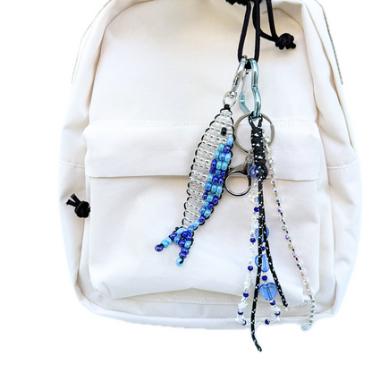 Beaded Blue Sardine Bag Charm clipped to a cream backpack,  styled with another y2k inspired layered charm, showing how the handmade keychain adds a playful yet stylish accent.