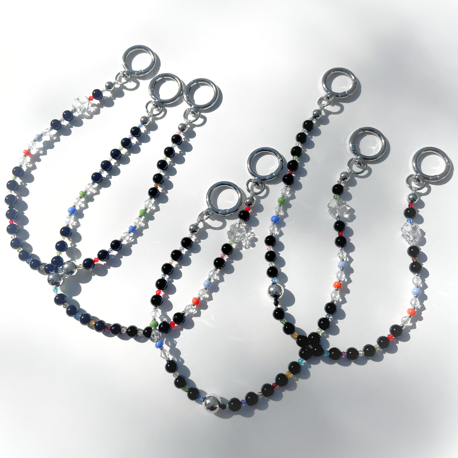 Multiple Black Orbit Beaded Bag Charms arranged on a white background, showcasing their glossy black beads, clear crystal accents, and colorful details under bright light.