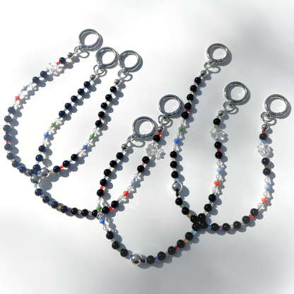 Multiple Black Orbit Beaded Bag Charms arranged on a white background, showcasing their glossy black beads, clear crystal accents, and colorful details under bright light.