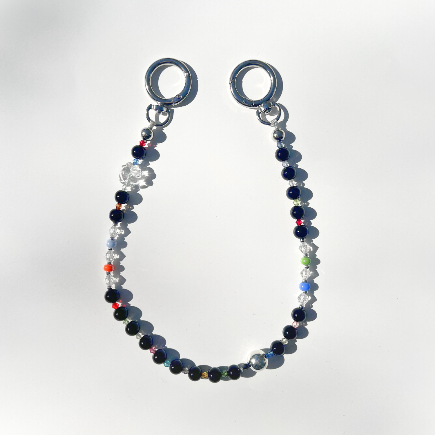 A single Black Orbit Beaded Bag Charm featuring glossy black and multicolor beads with silver circular clasps, displayed on a clean white background under natural sunlight.