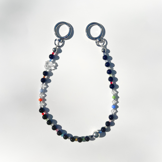 A single Black Orbit Beaded Bag Charm featuring glossy black and multicolor beads with silver circular clasps, displayed on a clean white background under natural sunlight.