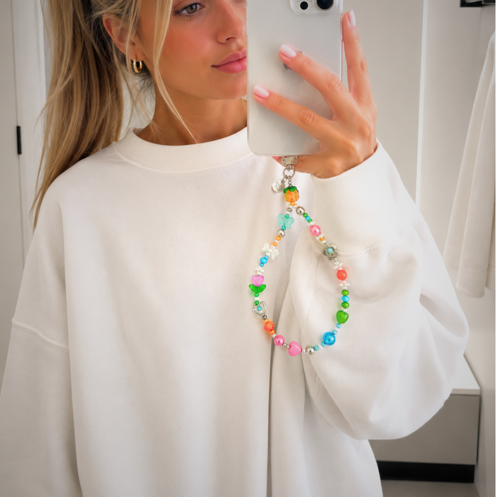 Person in a white sweater holding a phone with the colorful Garden Party beaded wristlet strap attached as a phone charm
