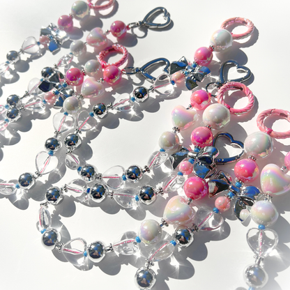 A close-up view of several Kawaii Pink Beaded Bag Charms, highlighting the reflective silver beads, iridescent hearts, and pastel pink accents glowing under sunlight.
